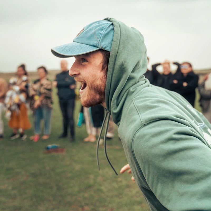Facilitator wearing a green hoodie and cap leading an outdoor group play workshop with energy, connection, and playful interaction.